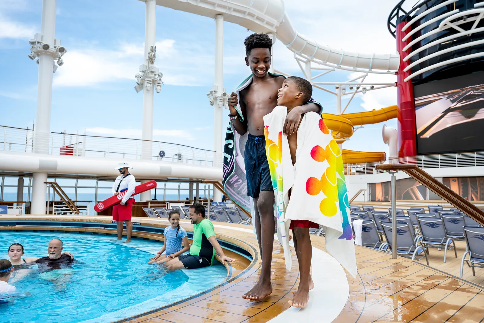 A sunny cruise ship pool deck with waterslide tubes overhead